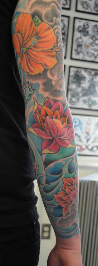 sleeve tattoo comprised of flowers, birds and a frog 